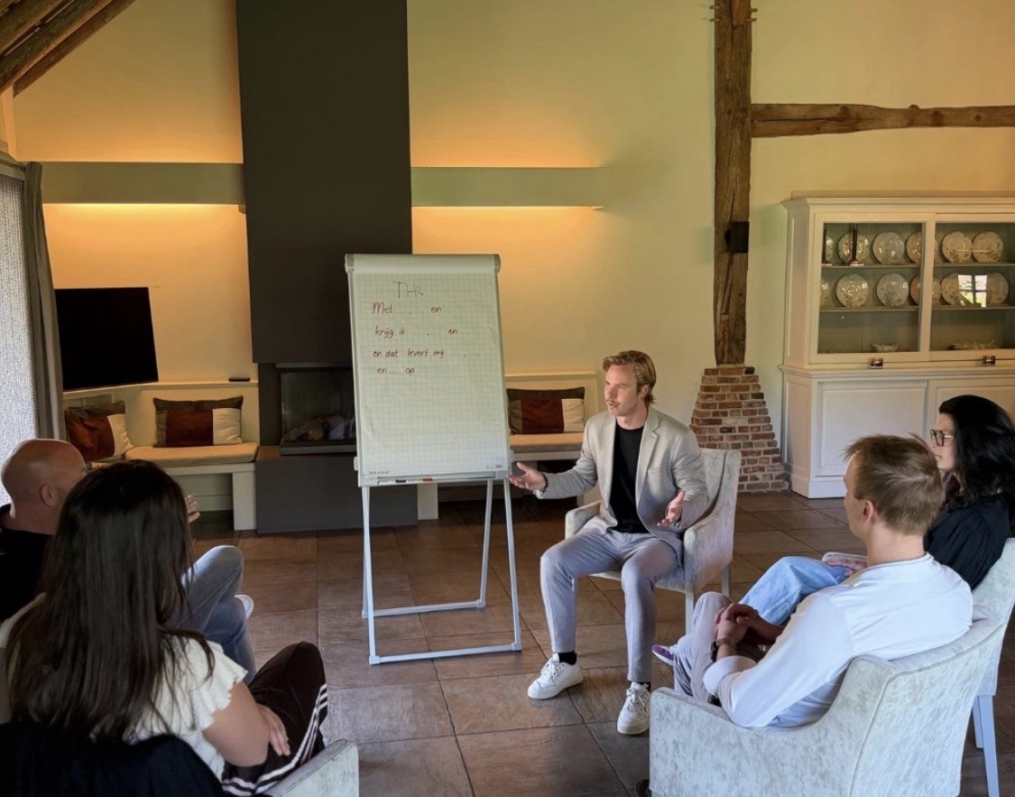 Jos leidt een groepssessie bij een flipchart; de deelnemers zitten in een kring om hem heen.